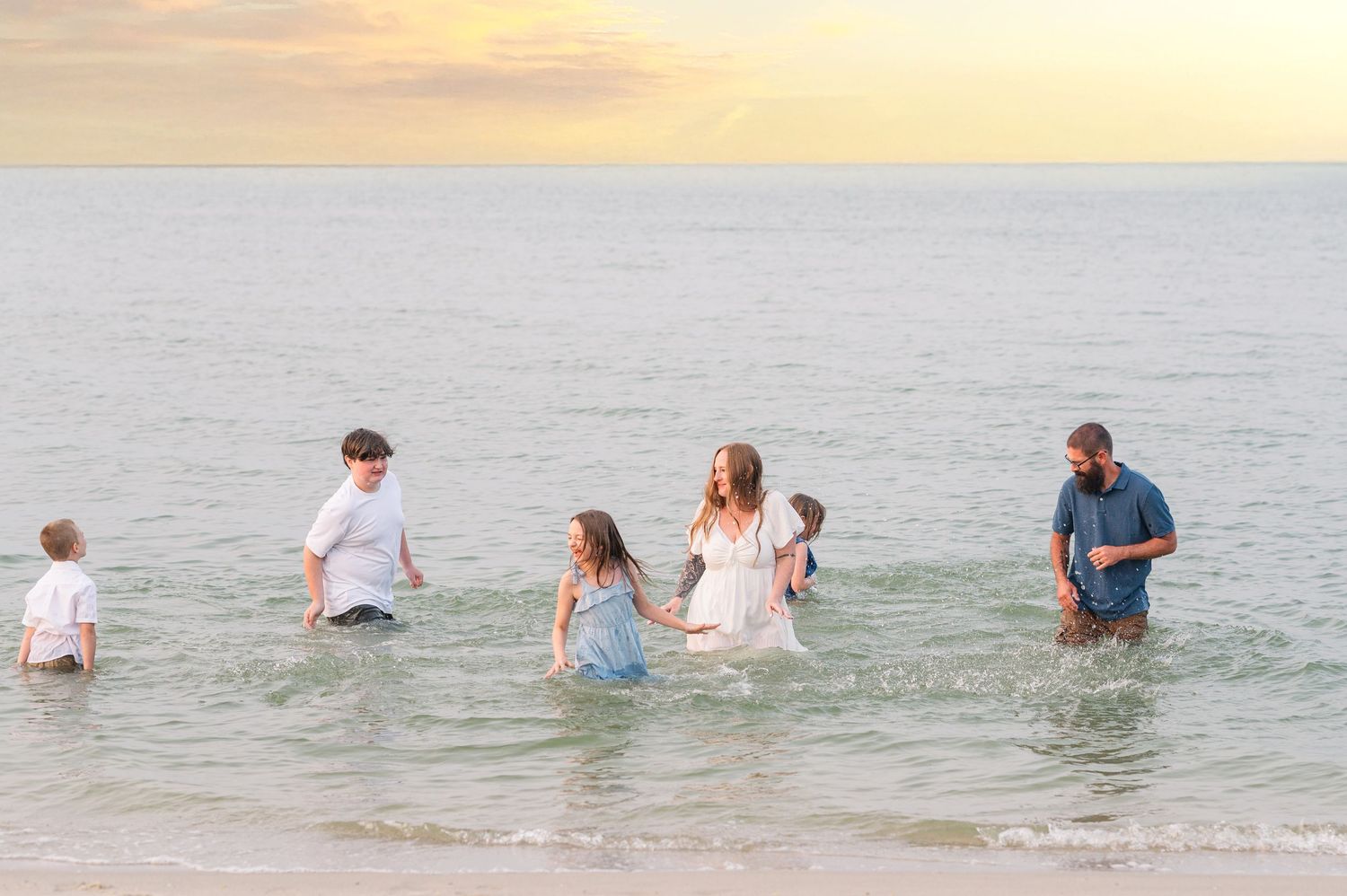 Family enjoying time together wading in ocean water during golden hour.