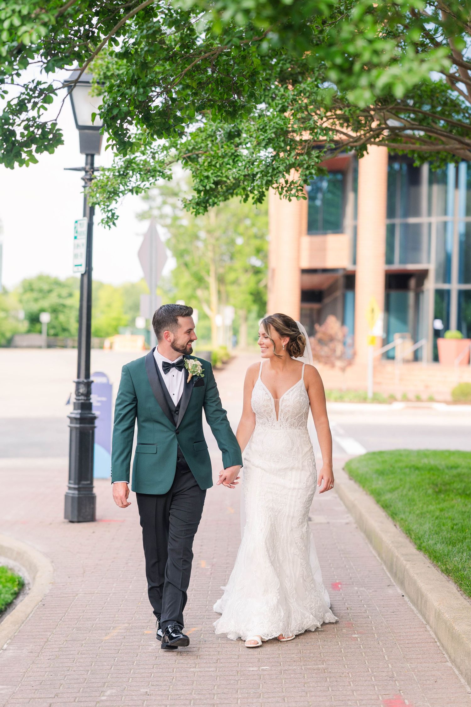 Wedding couple walking together on brick pathway surrounded by greenery and architecture.