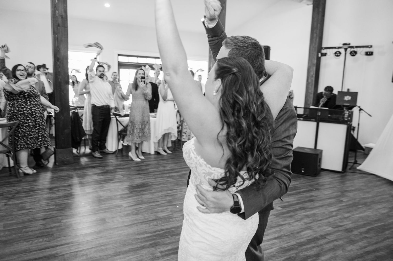 Bride and groom share an emotional first dance as wedding guests cheer in black and white photo.
