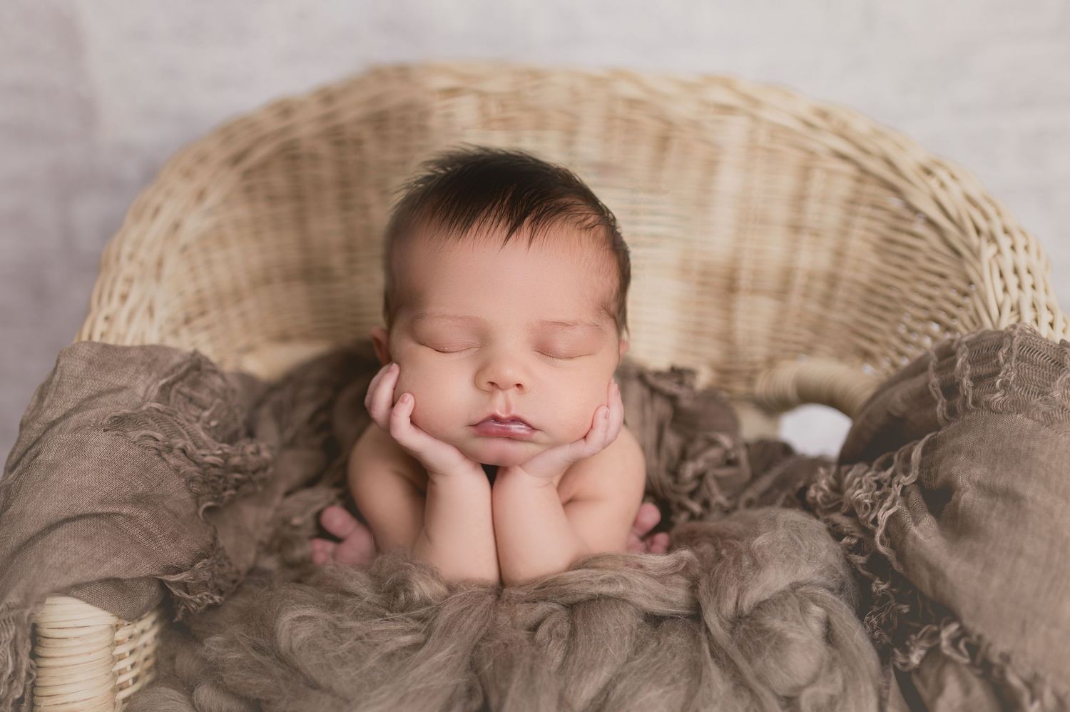A sleeping newborn baby lies peacefully on soft brown textured blankets in a professional studio setting.