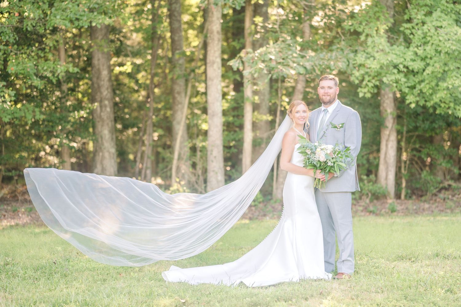 Wedding couple in garden setting with dramatic flowing veil and natural greenery.