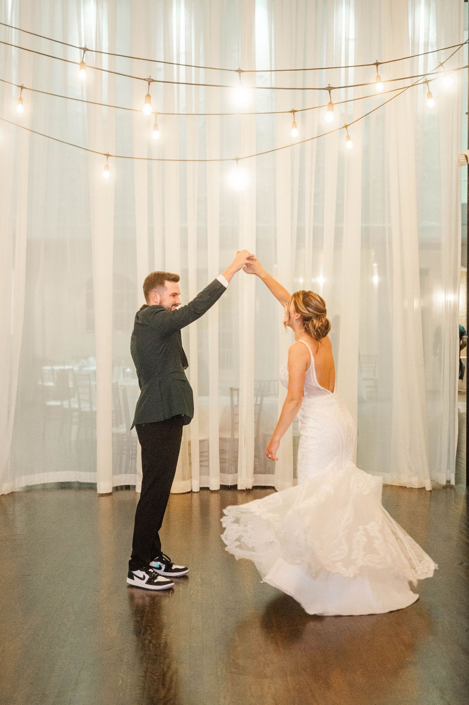 Dancing sequence in white venue with string lights and polished dark floors.