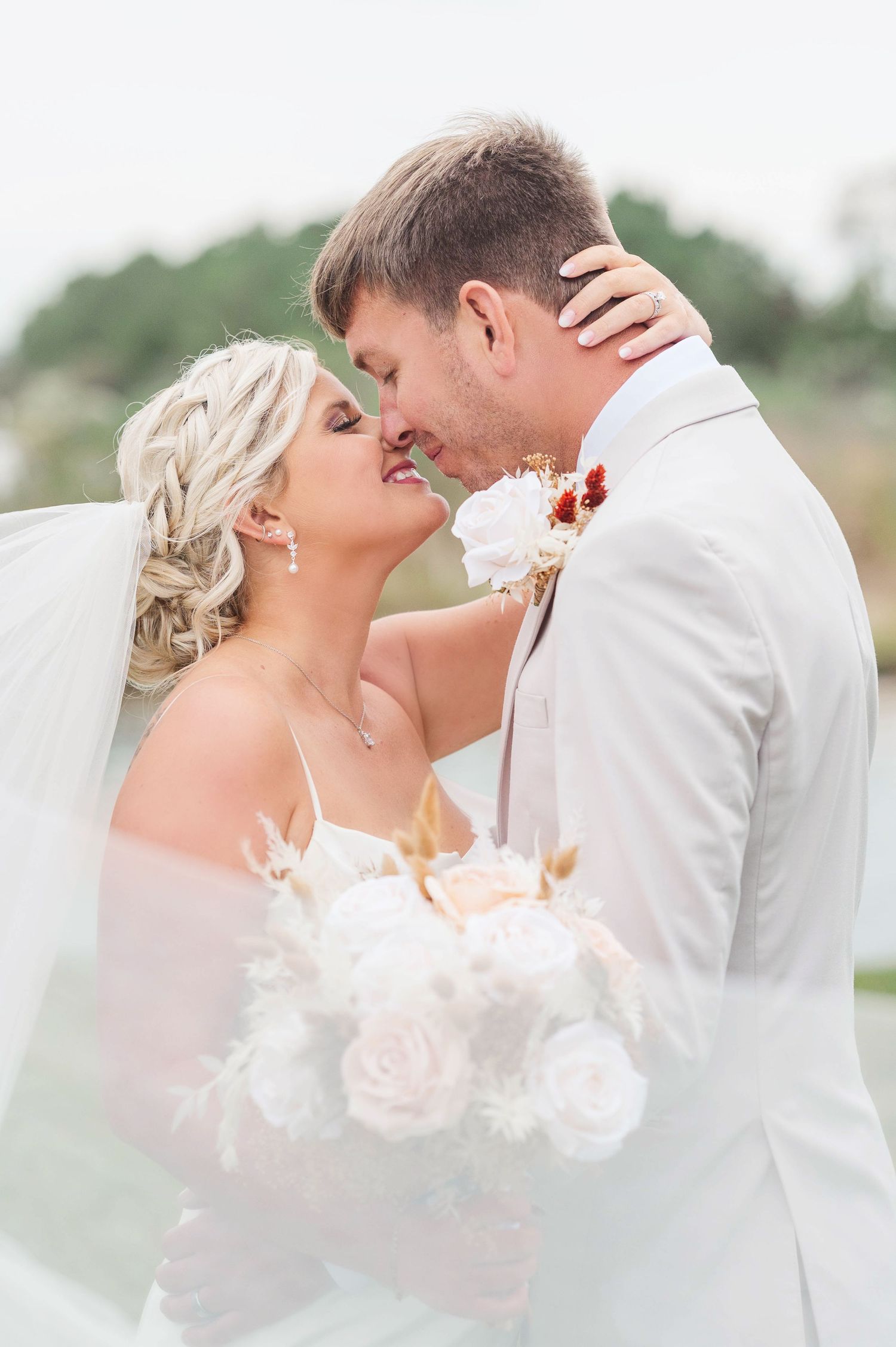 A romantic wedding portrait series showing a couple kissing behind a delicate blush-colored floral veil.