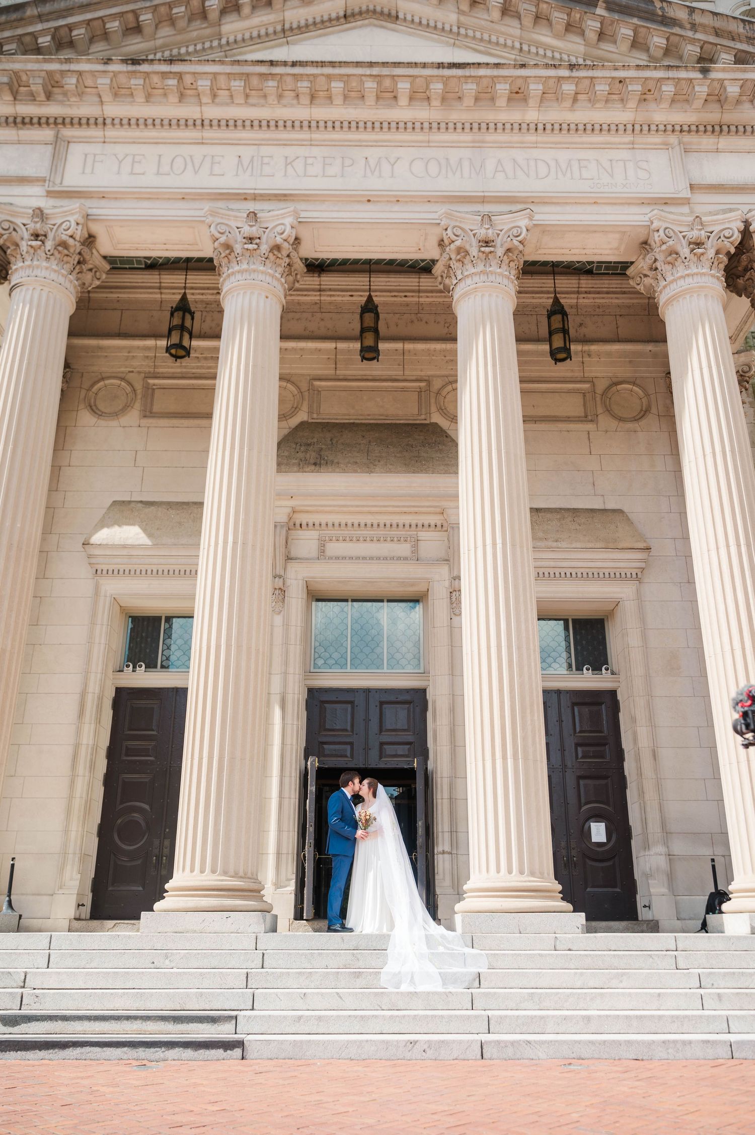 A grand neoclassical building with white columns serves as backdrop for a wedding photo.