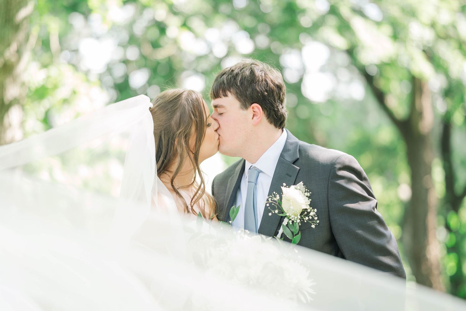 Wedding couple shares intimate moment in sunlit outdoor garden setting.
