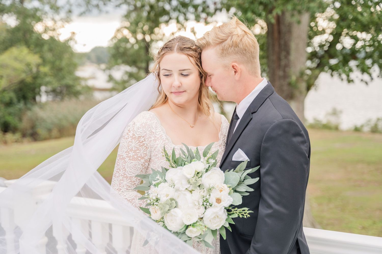 Intimate wedding portrait featuring white floral bouquet and flowing veil in outdoor setting.