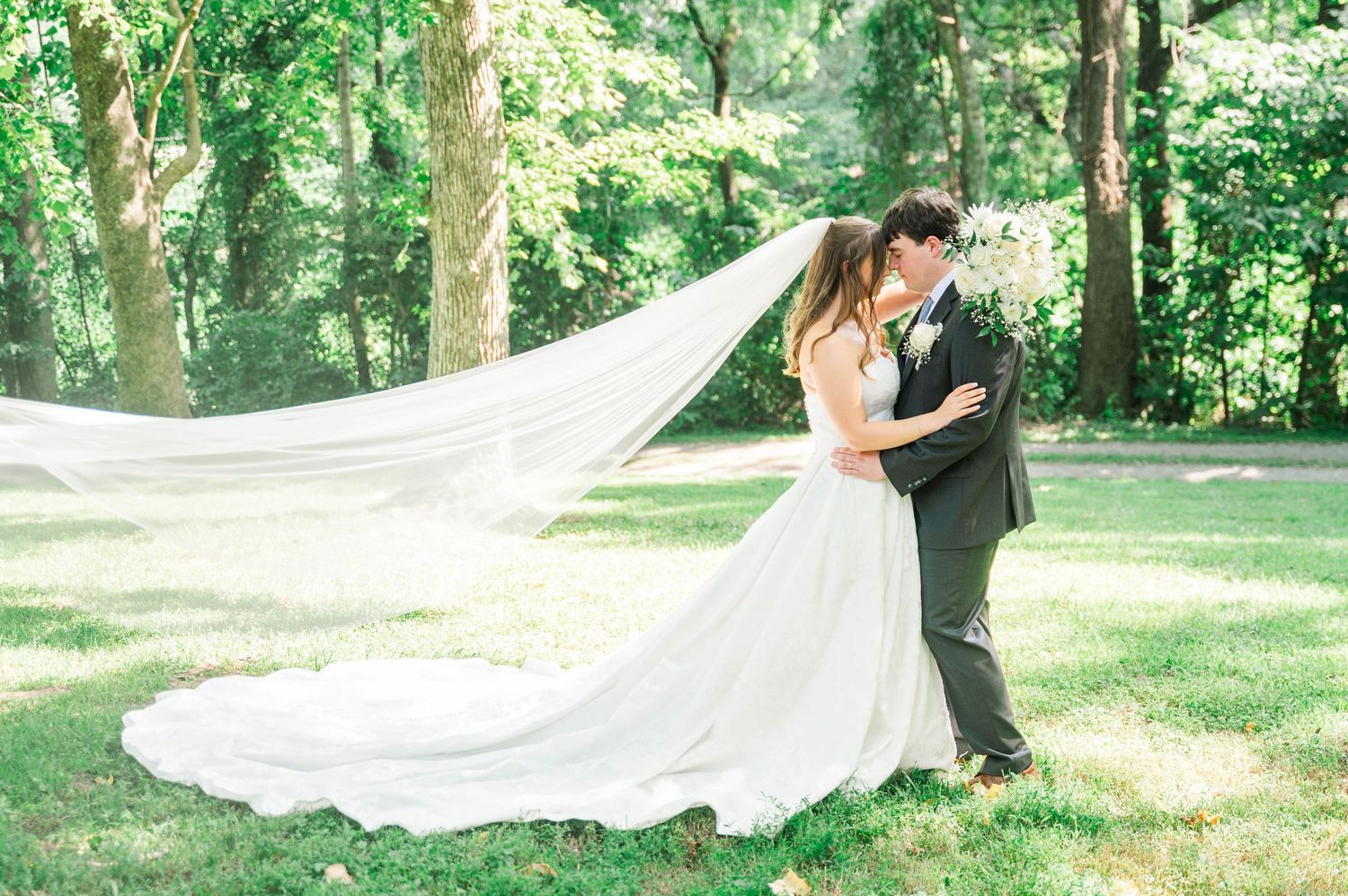 Long flowing wedding veil catches breeze in outdoor garden setting.