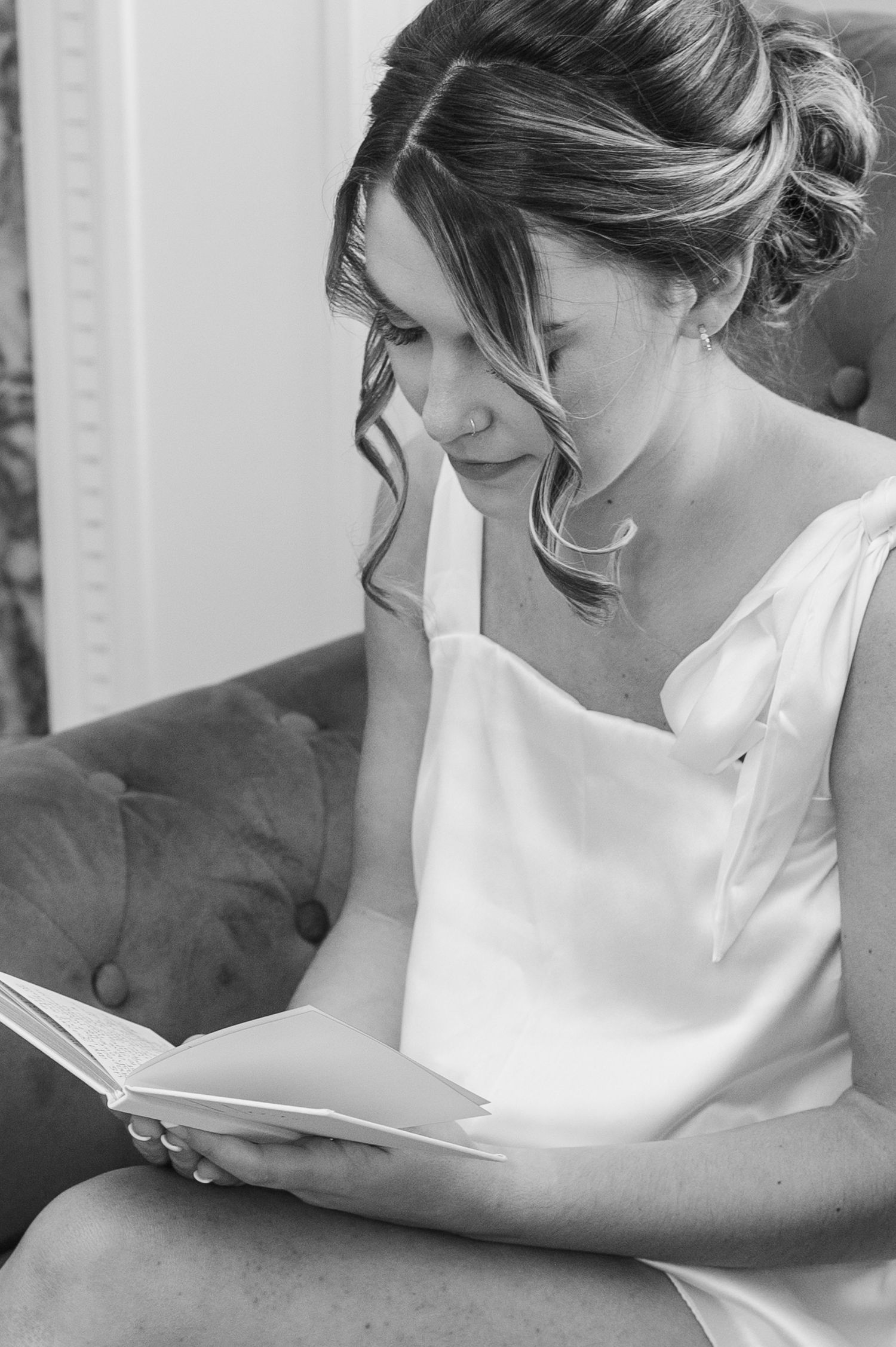 Candid black and white photo of bride reading during wedding preparations.