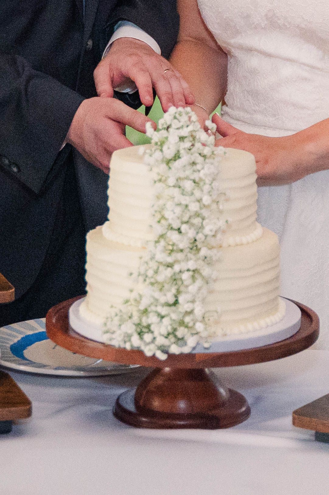 White wedding cake decorated with cascading baby's breath flowers on a wooden stand.