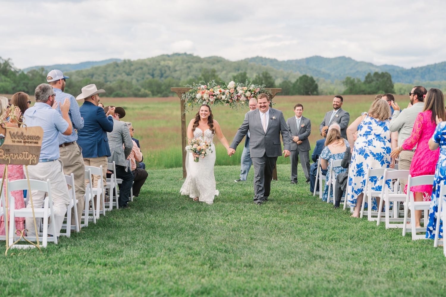 Newlyweds walk down the aisle after their outdoor ceremony with mountain views and floral arch behind them.