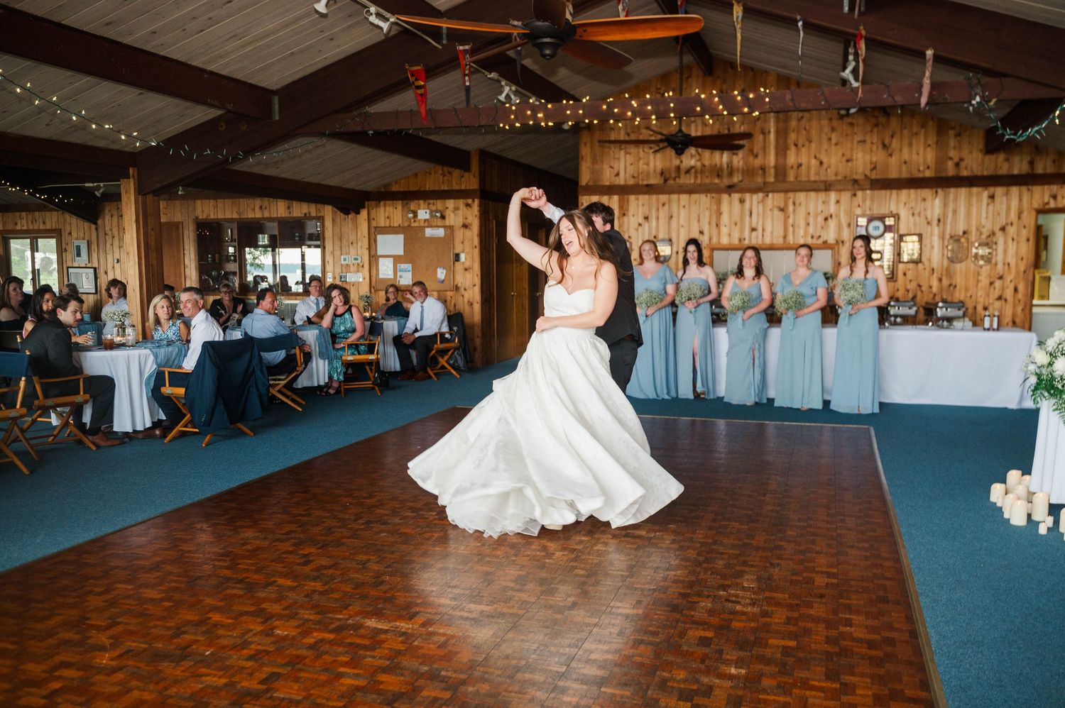 Wide view of a wedding reception first dance in a rustic barn venue with string lights.