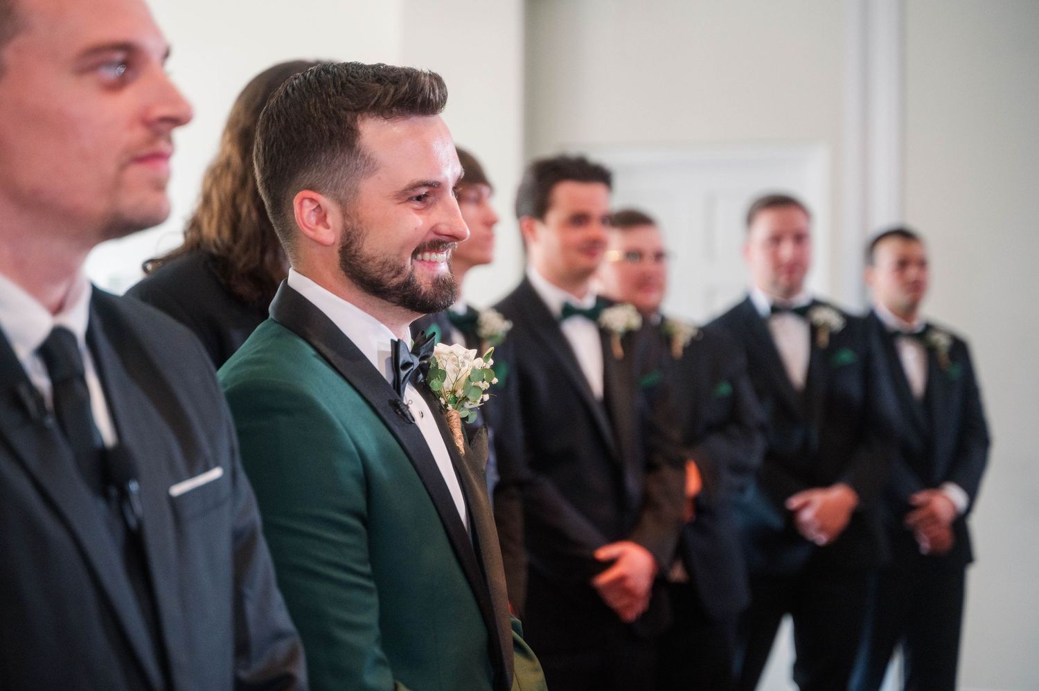 Wedding party members in dark suits and green jackets stand together during celebration.