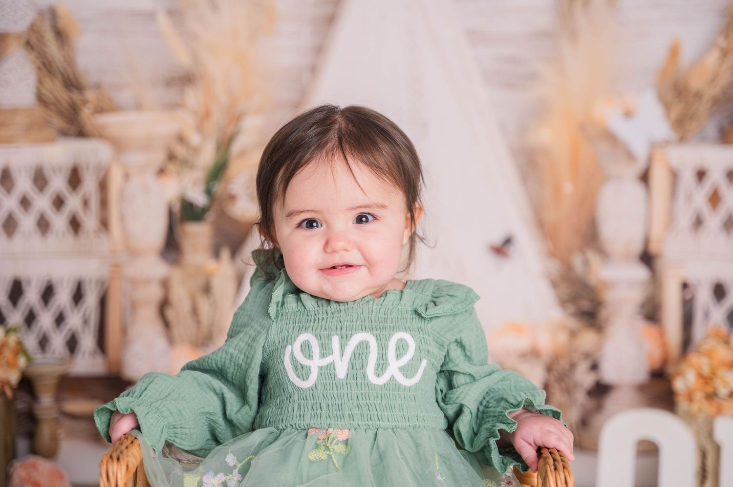 Baby in green dress sitting among fall decorations for a festive photo session.