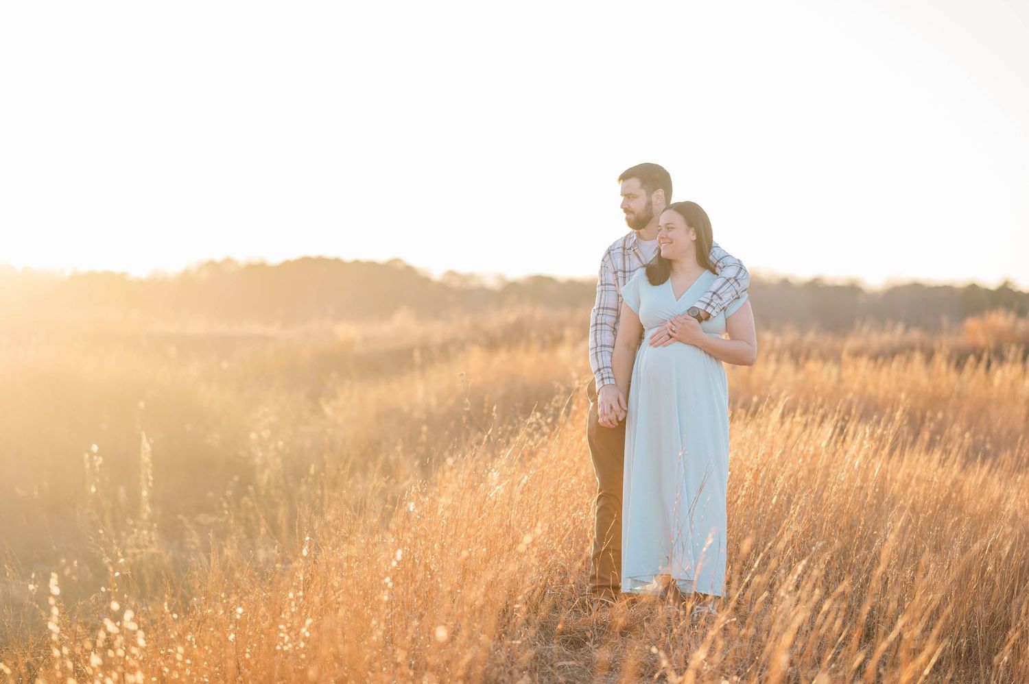 Romantic maternity session. Embracing in a sunlit meadow during golden hour.