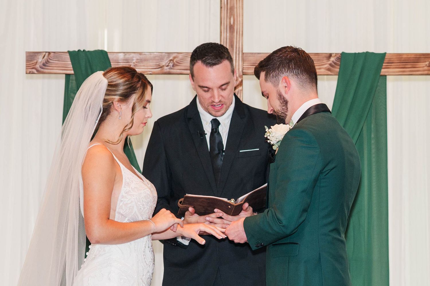 Wedding ceremony with attendees in formal attire and emerald green dresses gathered indoors.