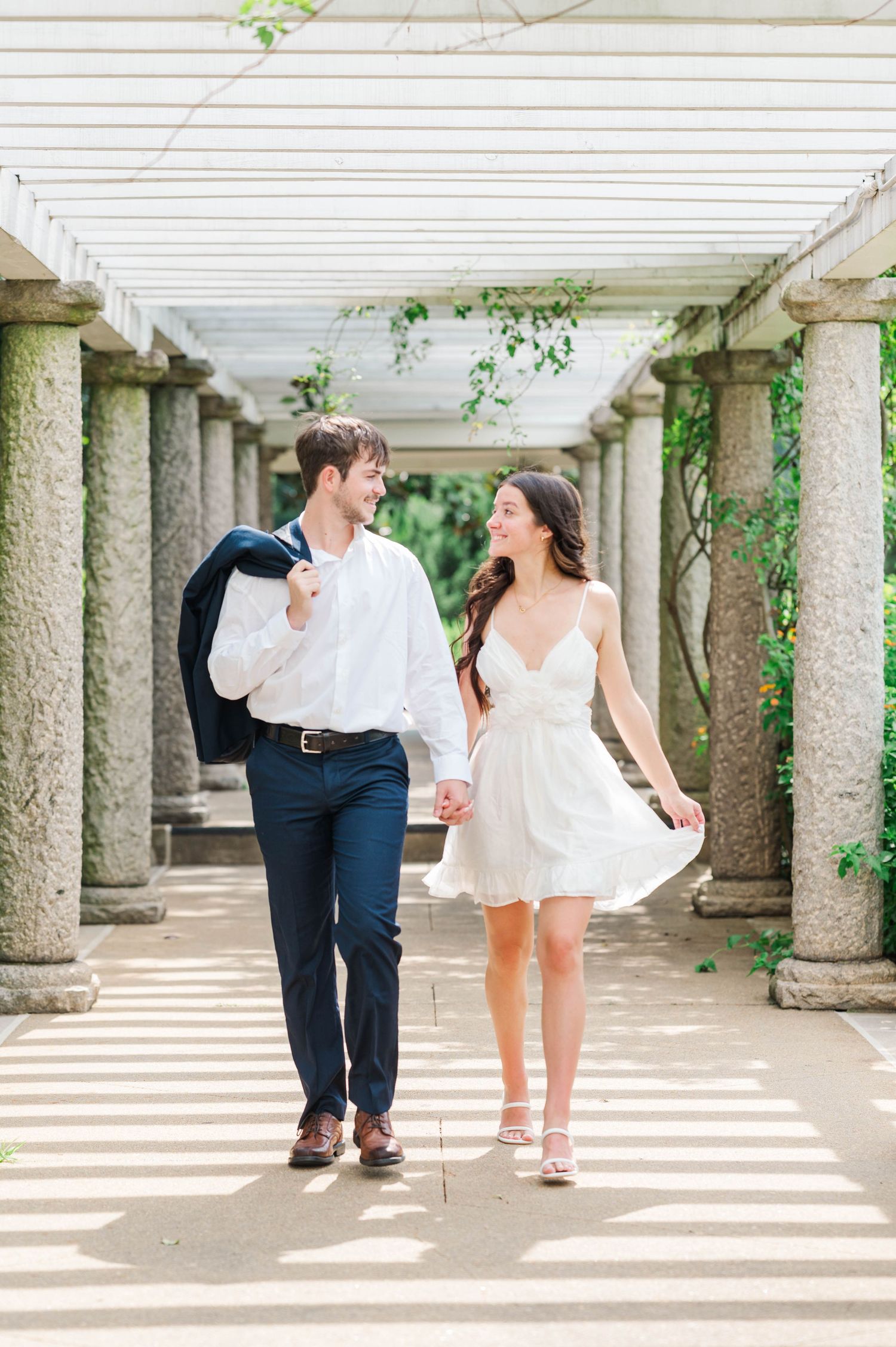 Engagement photos in a white columned pergola with natural lighting.