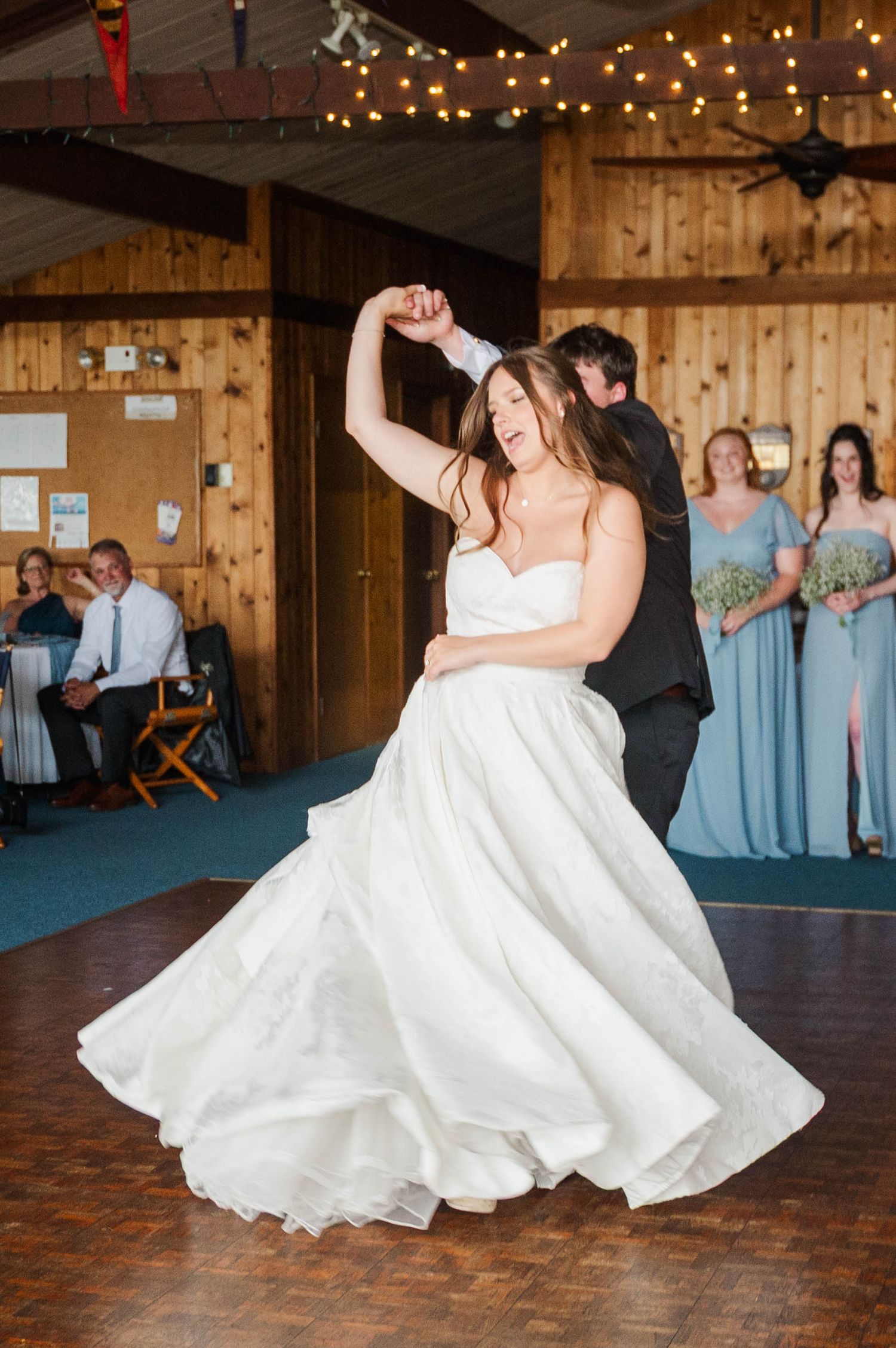 Wedding couple spins gracefully during their first dance on a wooden floor.