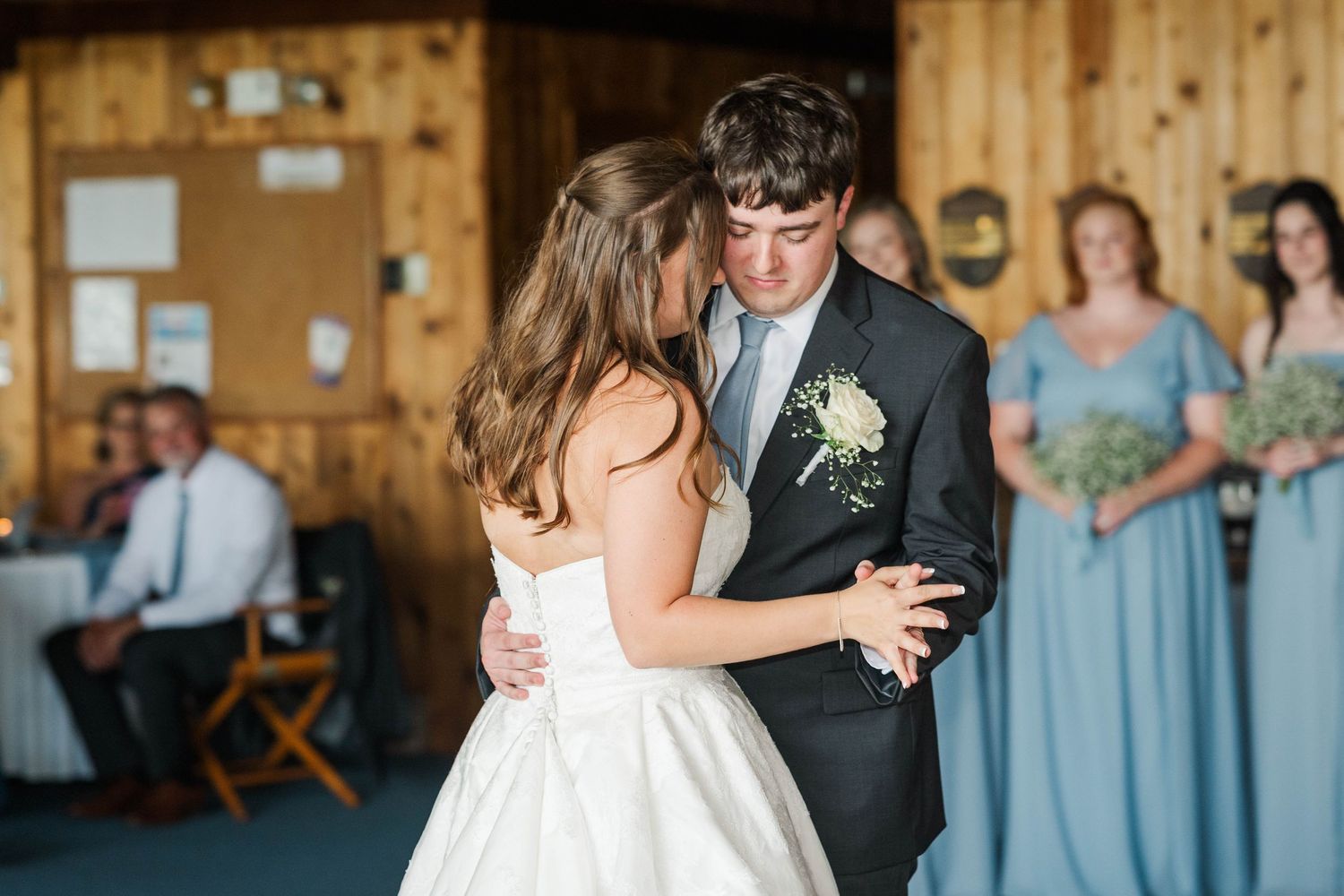 Couple shares their first dance in a rustic wooden venue decorated with string lights.