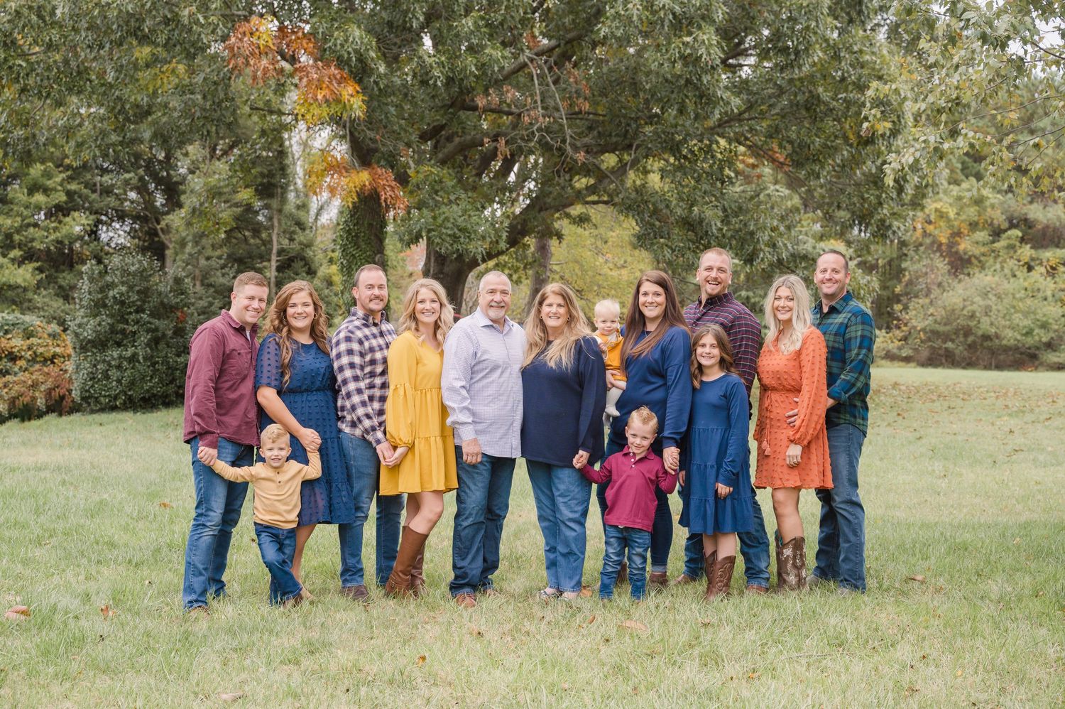 Extended family gathered for outdoor portrait session on grassy hillside in casual attire.