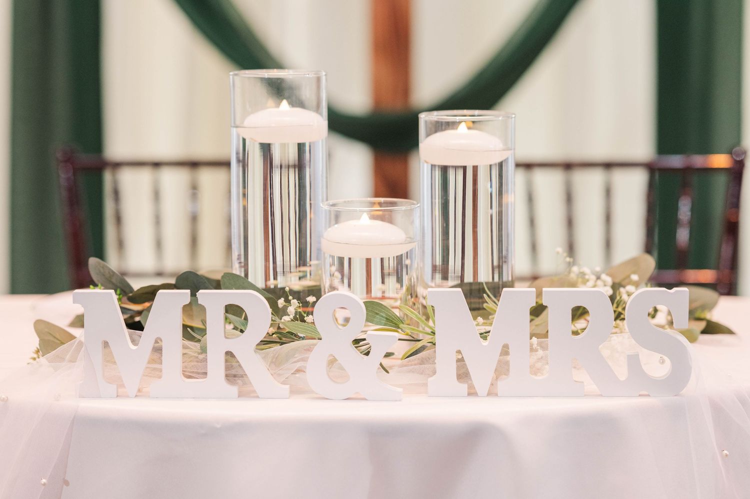 Wedding reception decor featuring silver 'Mr & Mrs' text display on white tablecloth.