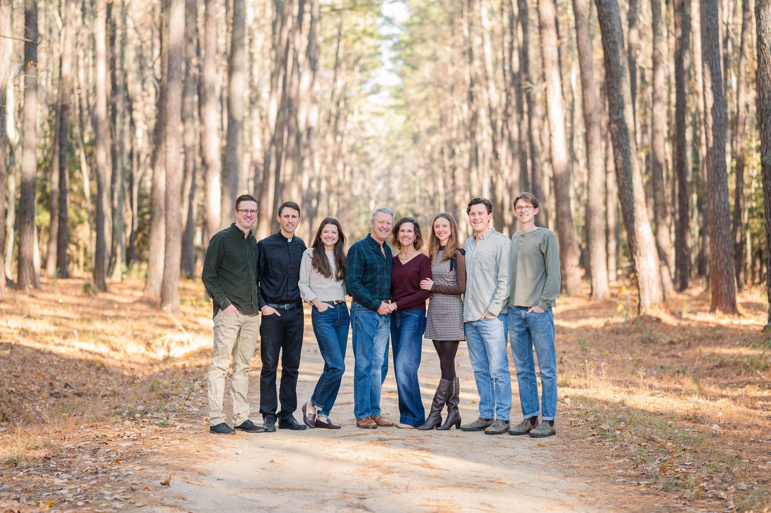 A family stands together on a path through tall pine trees on a sunny autumn day.