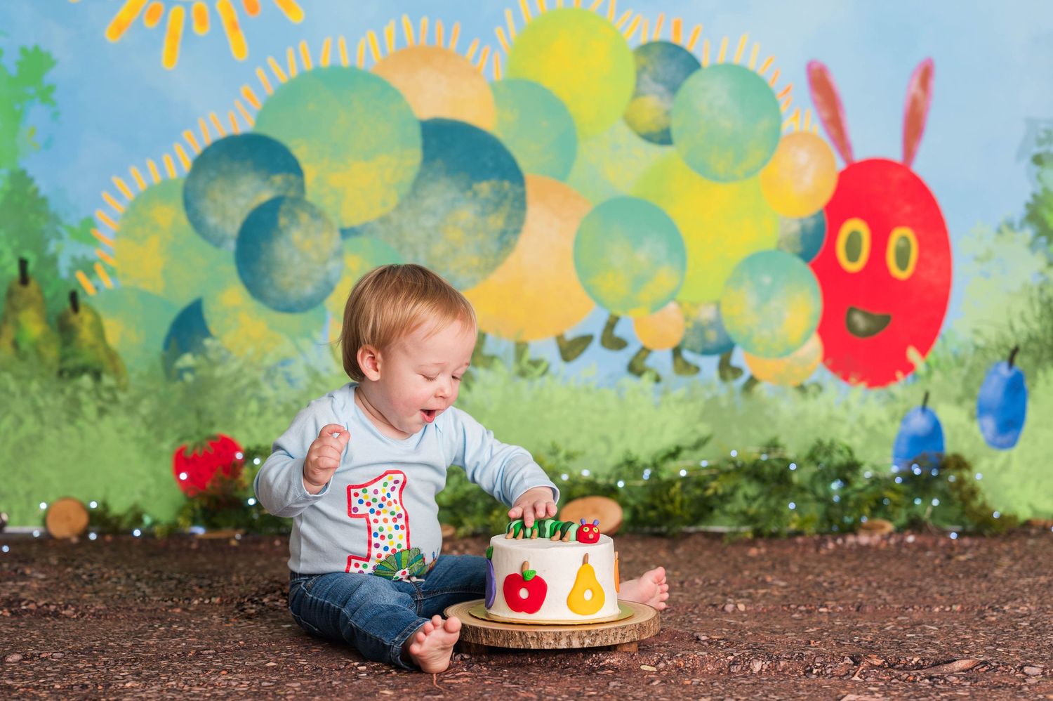 Baby exploring colorful outdoor setting with Very Hungry Caterpillar themed backdrop.