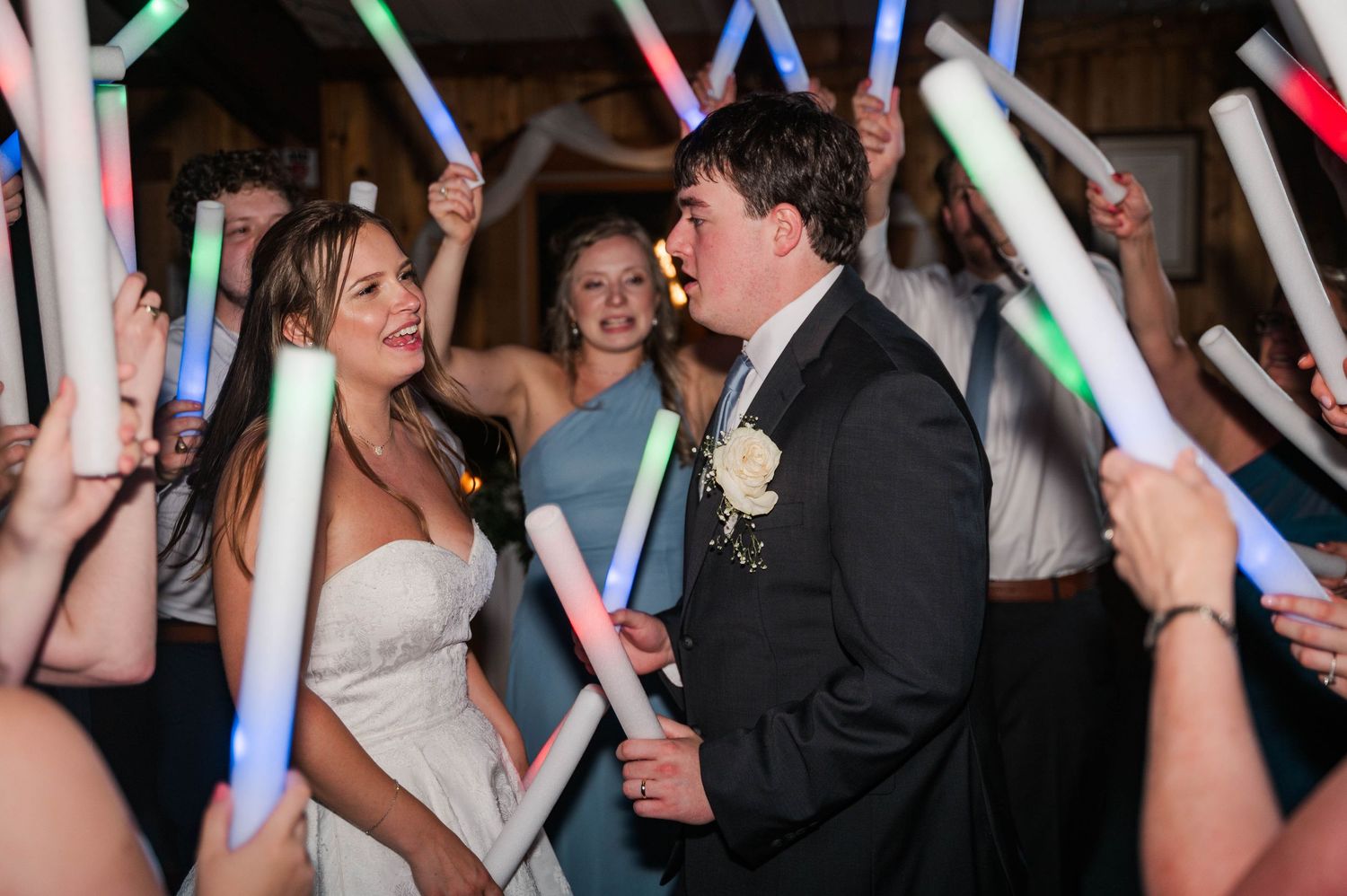 Energetic wedding celebration with guests dancing and holding glowing neon light sticks.