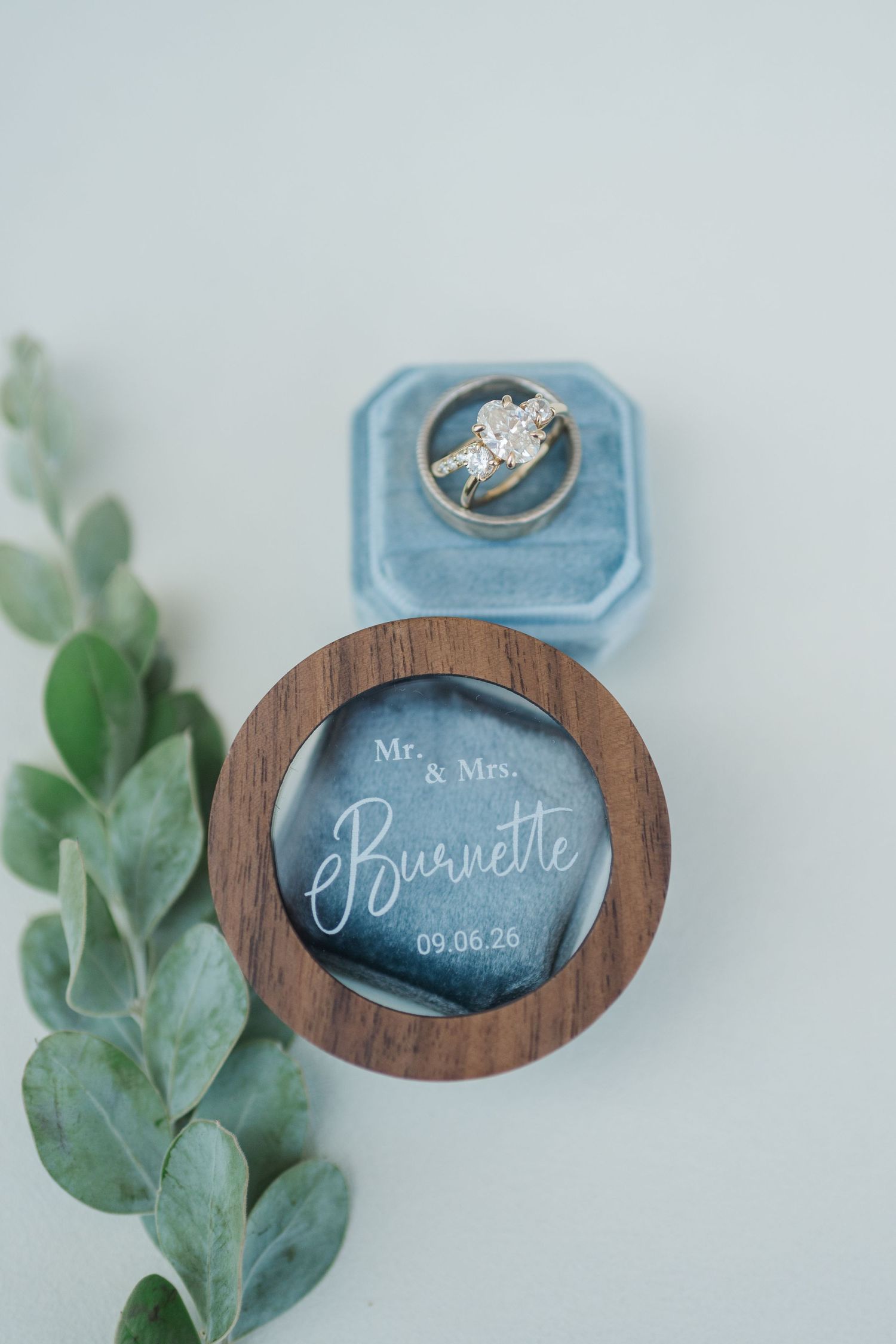 Elegant wedding ring set in blue velvet box beside personalized wooden ring dish engraved Mr. & Mrs. Burnette 09.06.26.