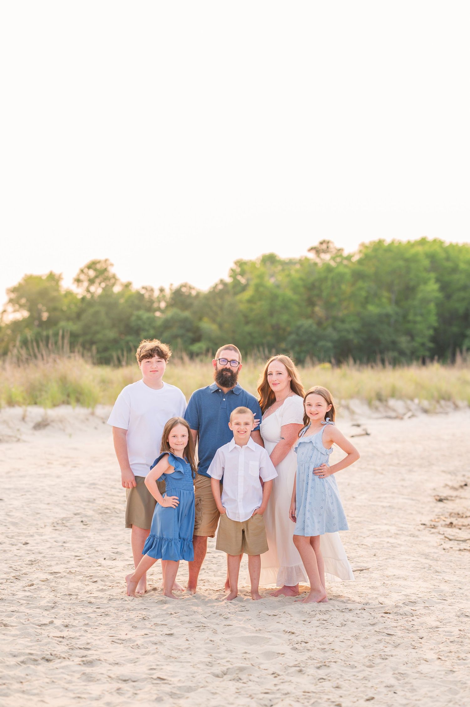 Family group portrait on sandy beach at sunset wearing coordinated blue and white outfits.