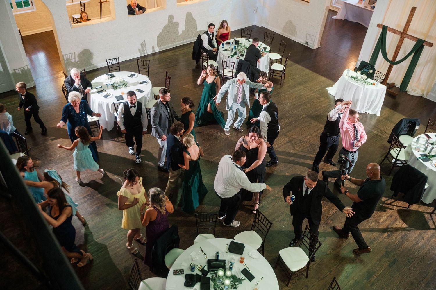 Wedding guests dancing and mingling at an indoor reception venue with festive lighting.