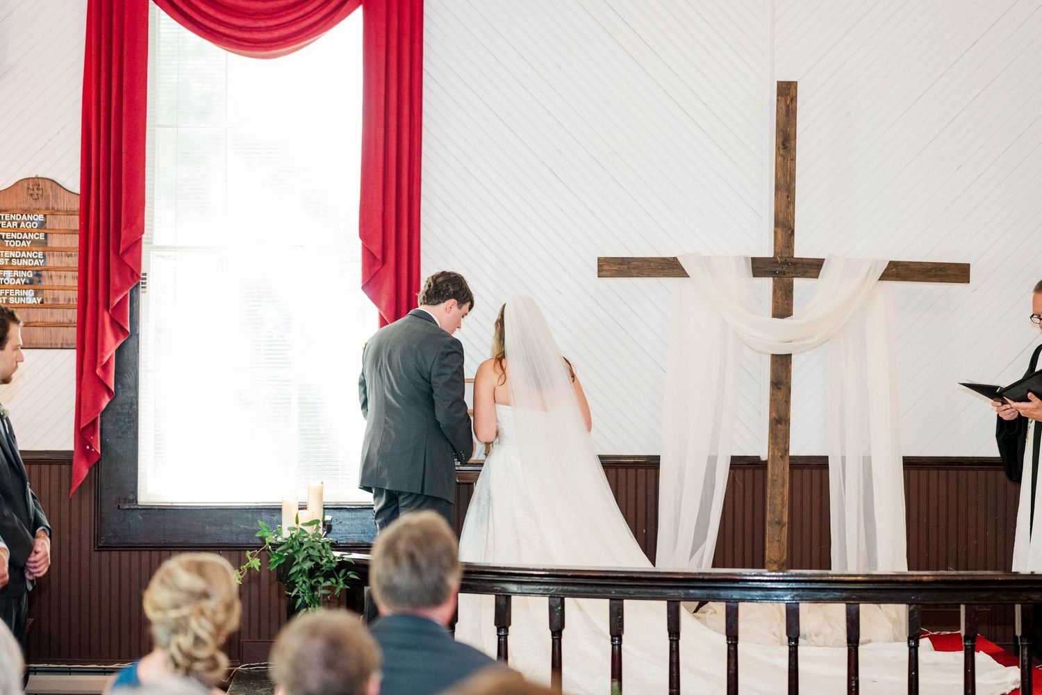 Wedding ceremony in a church with red curtains and wooden cross on display.