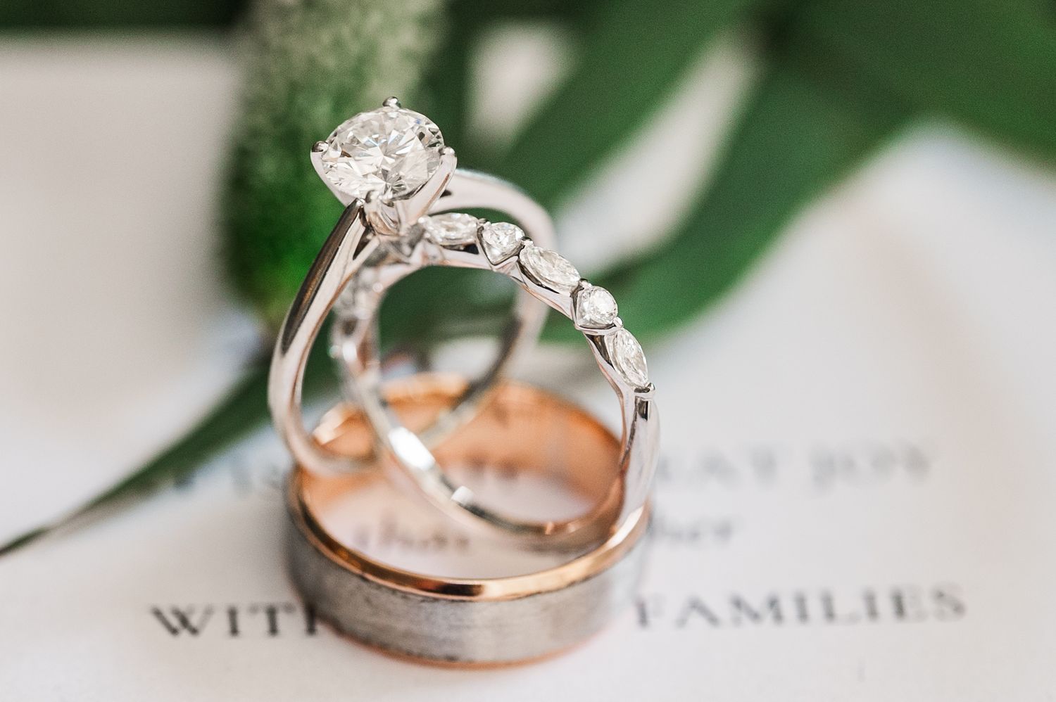 Wedding rings photographed on invitation with green leaf detail.