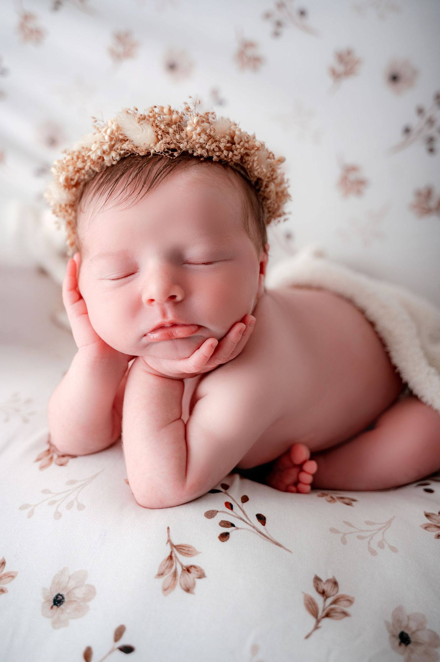 Sleeping newborn posed on floral backdrop wearing delicate dried flower crown.