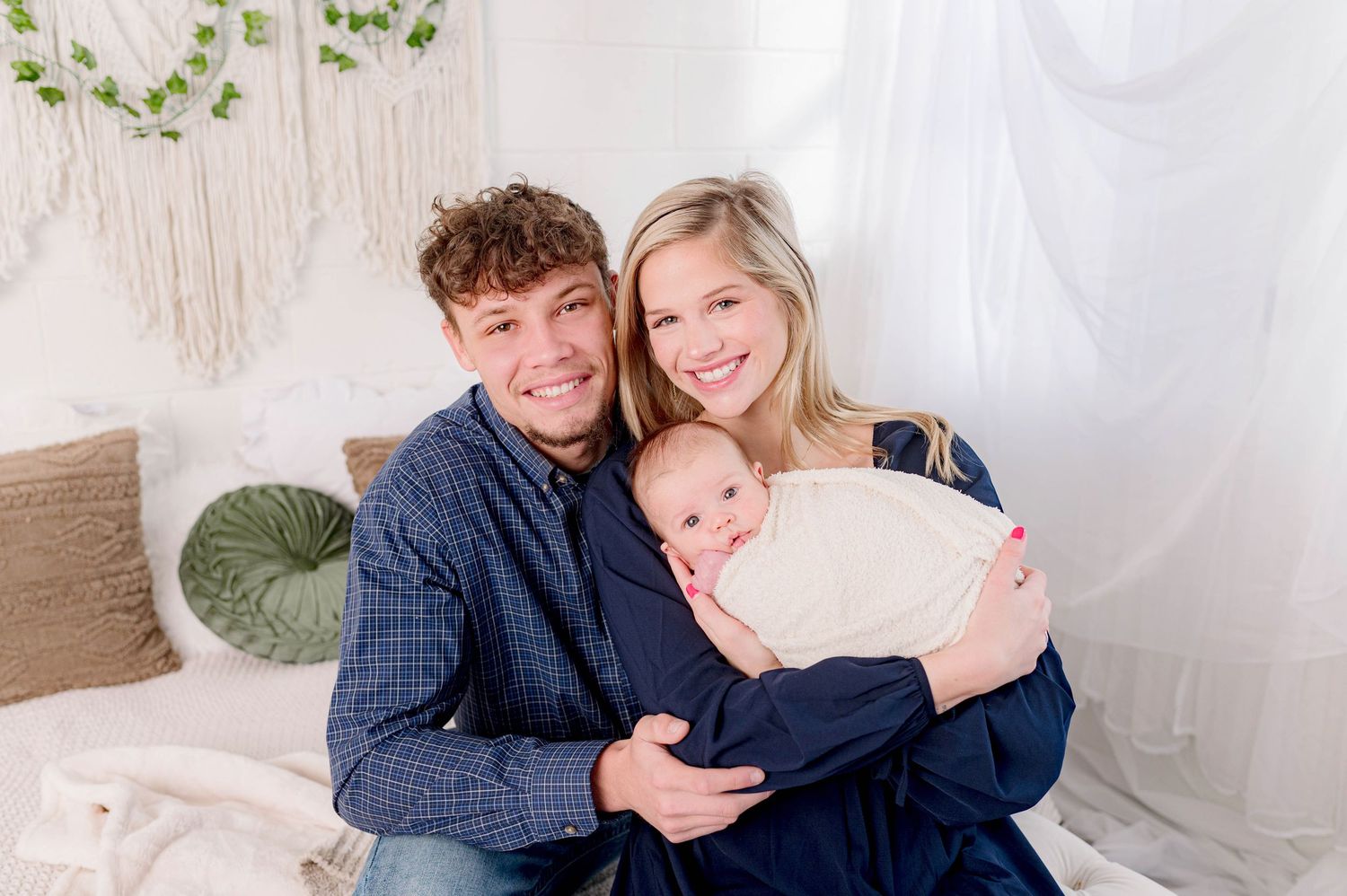 Couple cuddling on white couch with greenery decor in background.