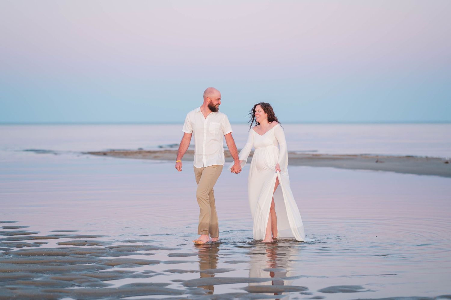 Couple standing in shallow water during sunset beach photoshoot.