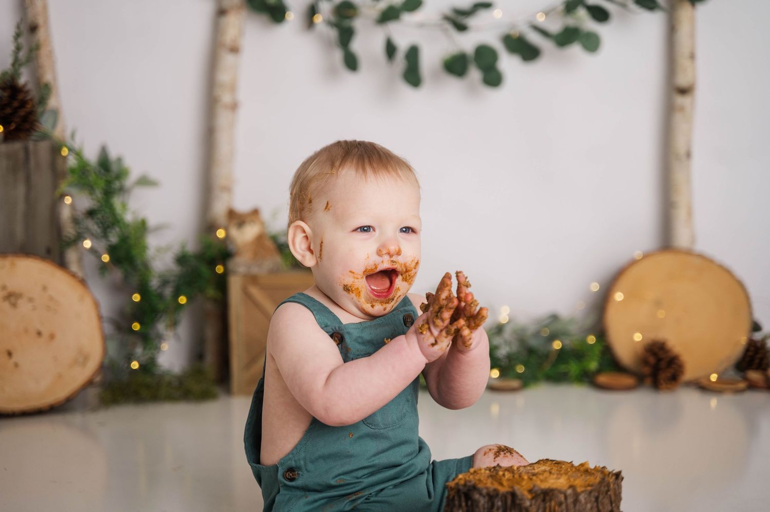 Child enjoying cake smash session with chocolate cake in forest-themed setting.