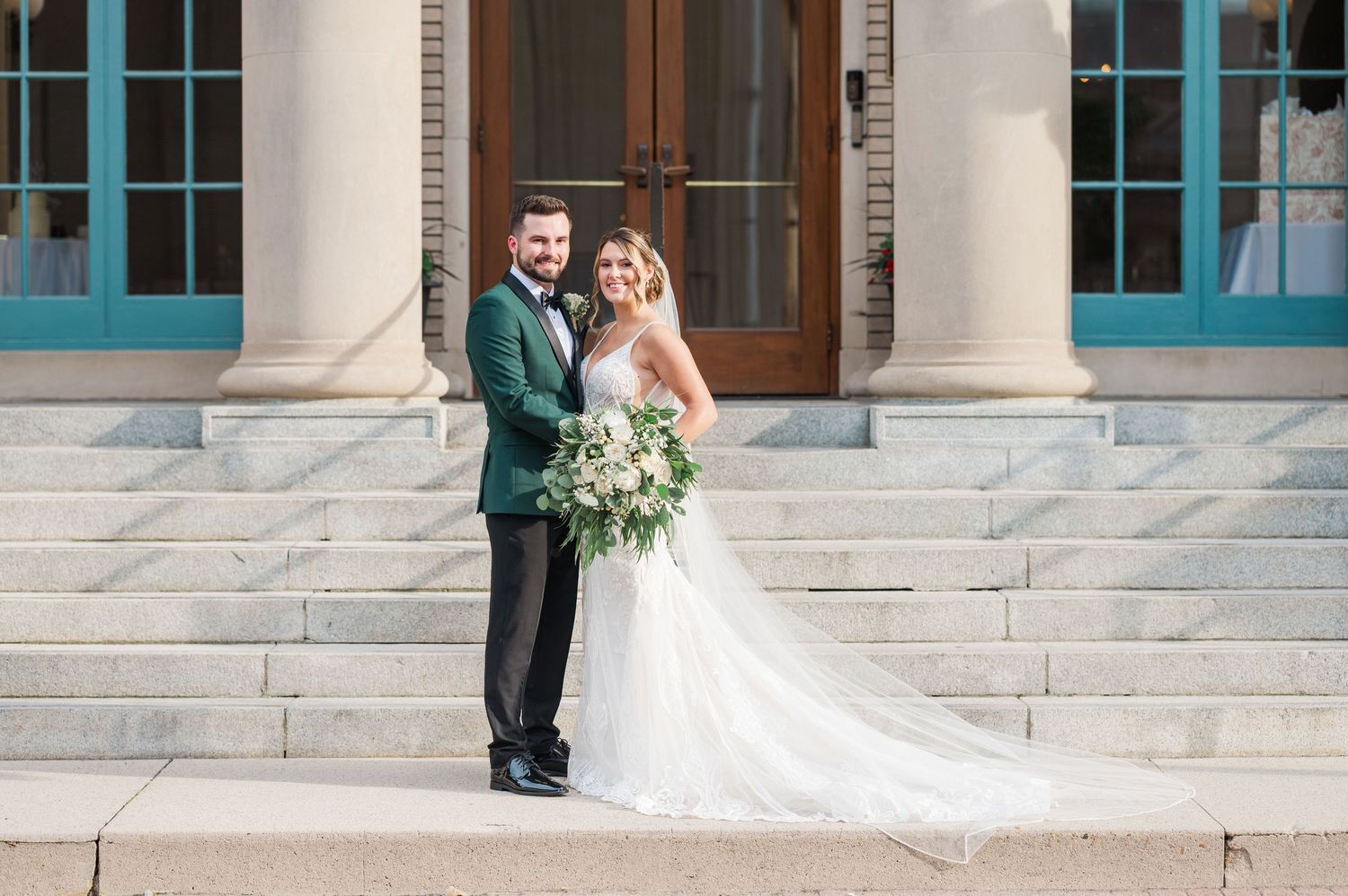 Wedding couple standing on stone steps of classical building with white columns.