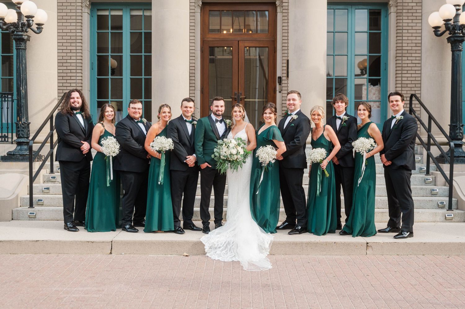 Wedding party posed on stone steps of historic building with emerald green bridesmaid dresses.