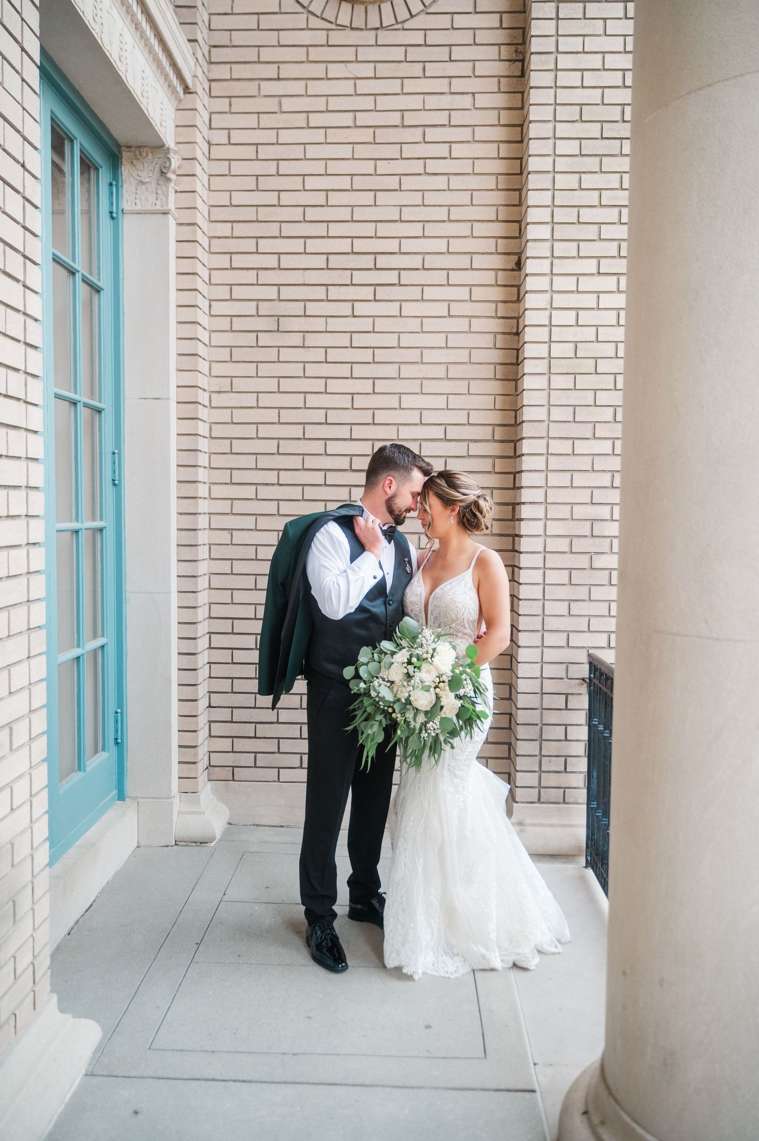 A couple embraces in an elegant colonnade with turquoise accents and brick walls.