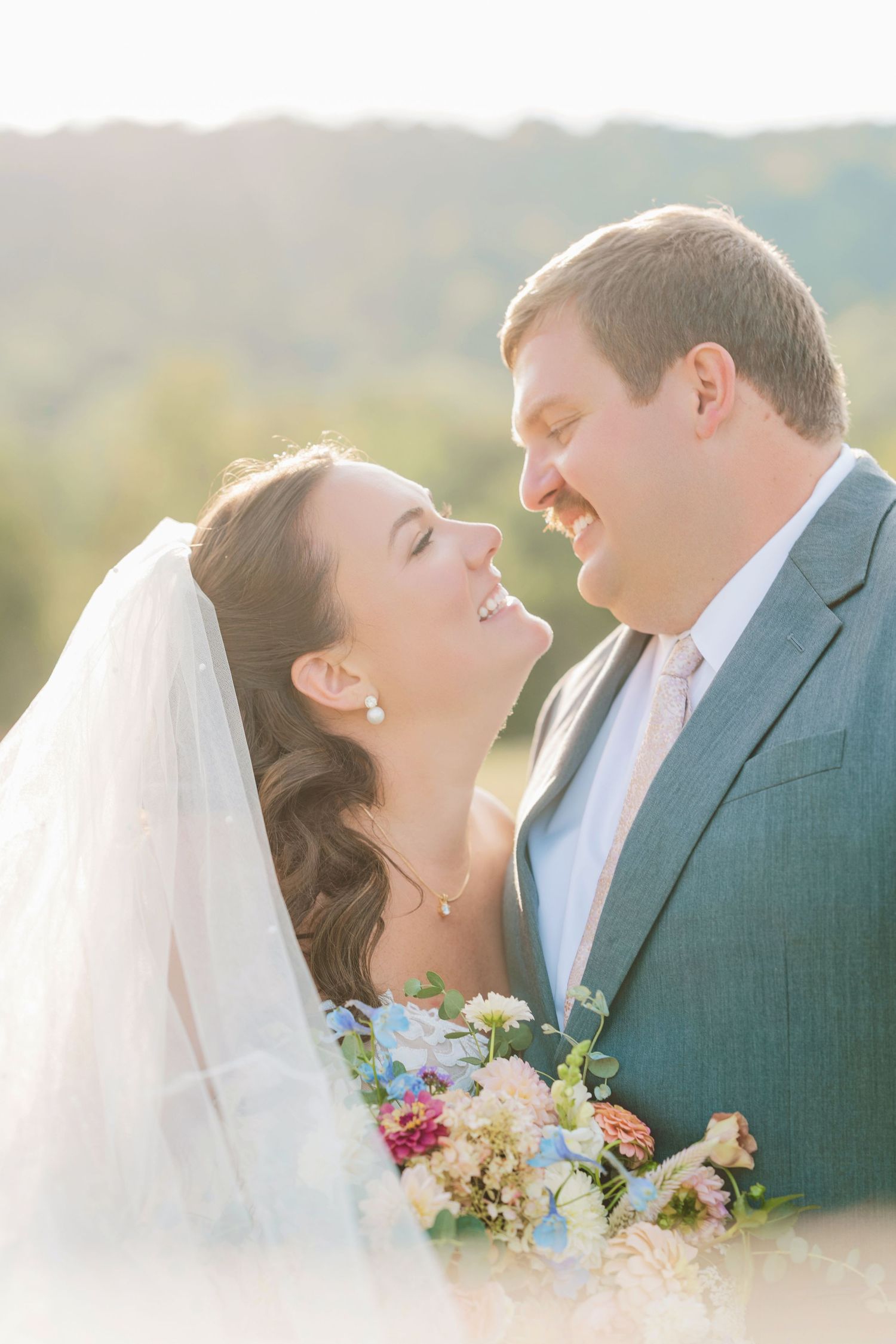 Bride and groom share a romantic moment outdoors, bride holding a colorful bouquet, soft golden light in background.