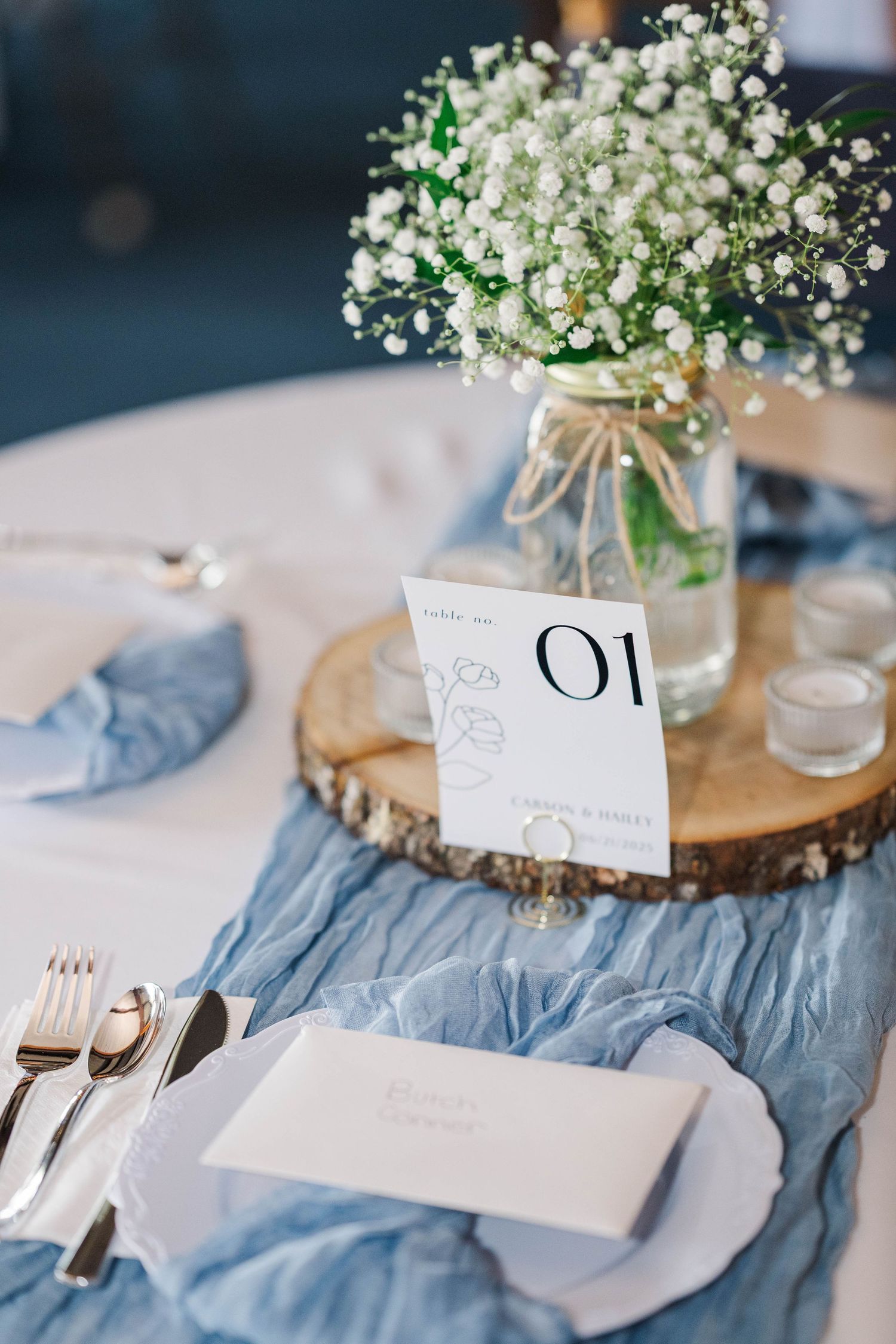 Wedding reception table setting with baby's breath centerpieces and dusty blue accents.