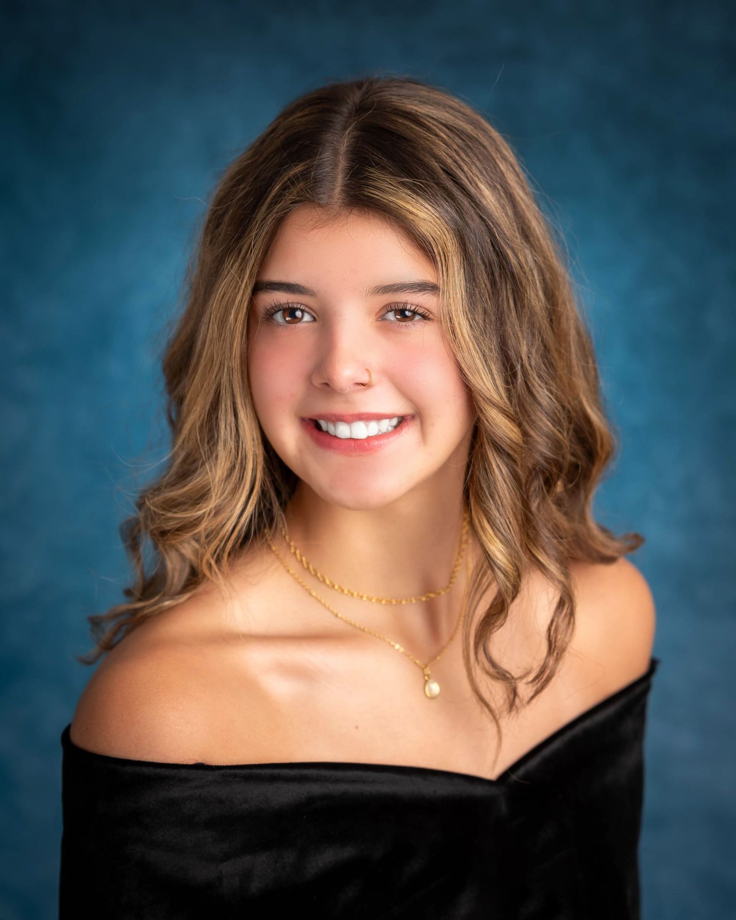 Portrait against blue backdrop features warm smile and off-shoulder black top.