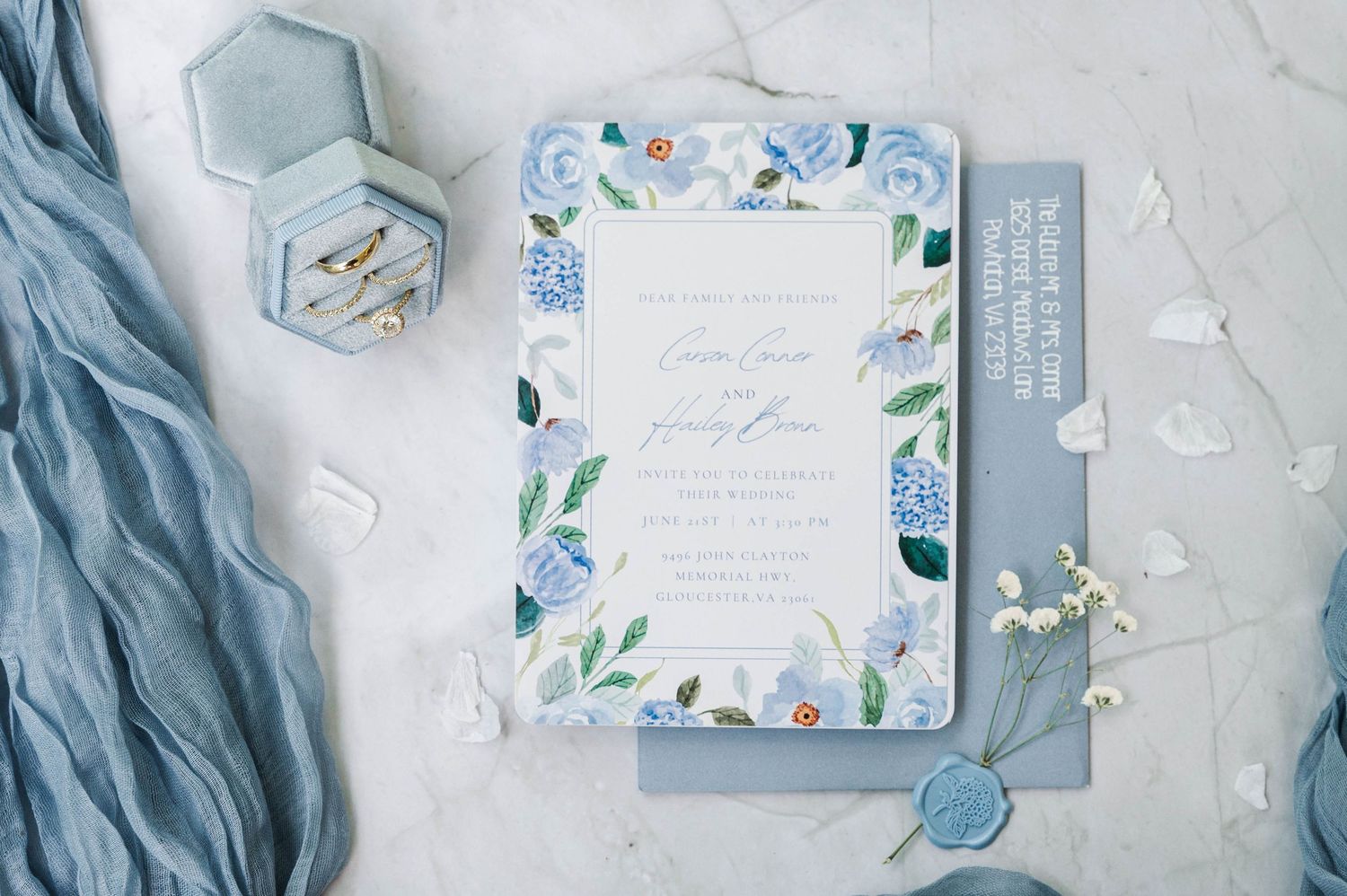 Wedding invitation suite featuring watercolor florals and blue accents on marble background.