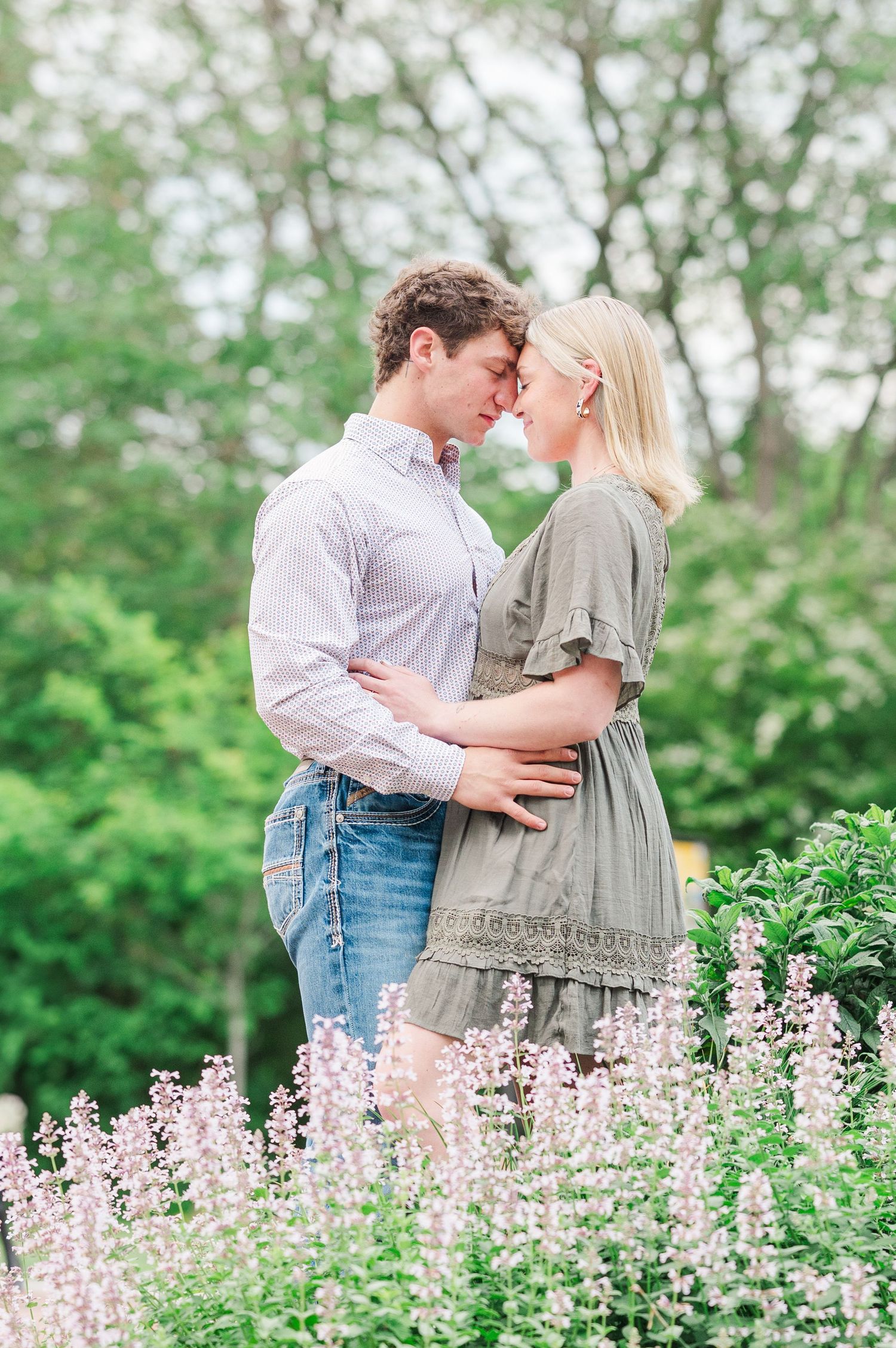A romantic couple shares a tender moment among blooming pink wildflowers in a garden setting.