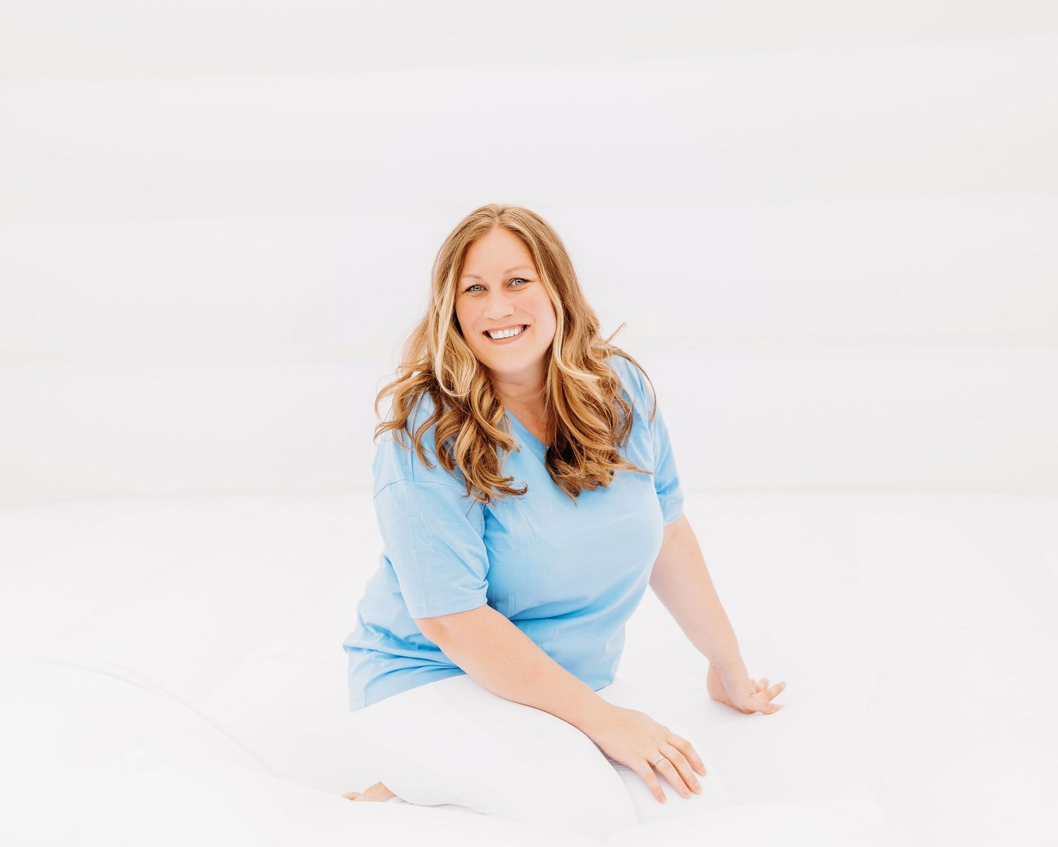 Woman in light blue top reclining on white background with natural lighting.