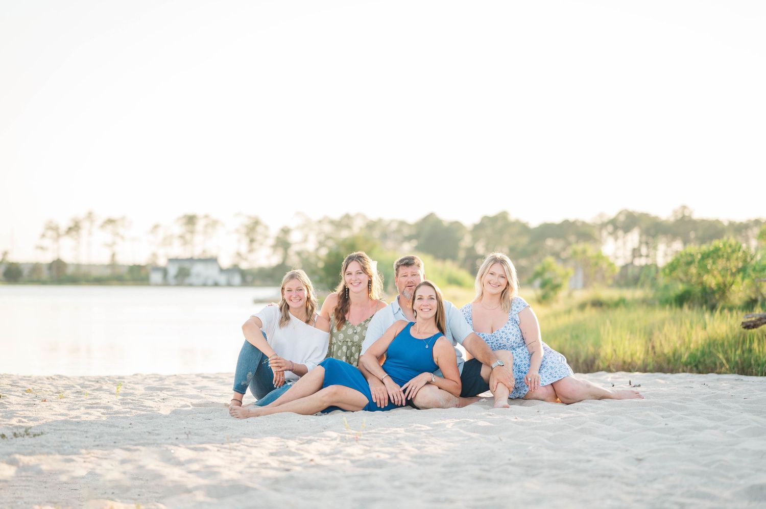 Family members lay together on beach sand during a sunset photography session.