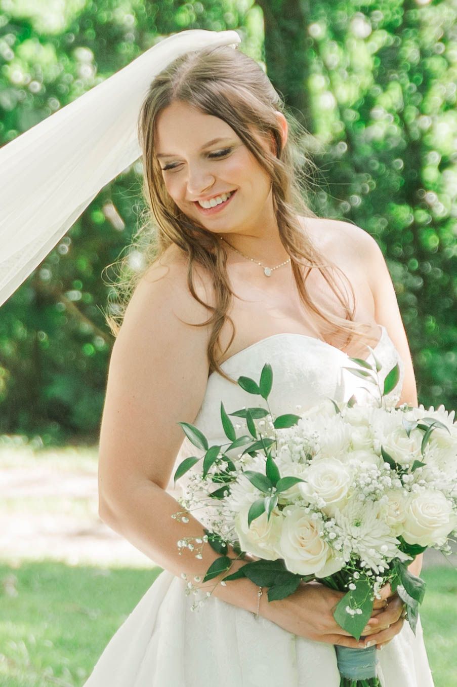 Close-up of bridal bouquet with white roses and greenery against soft natural lighting.