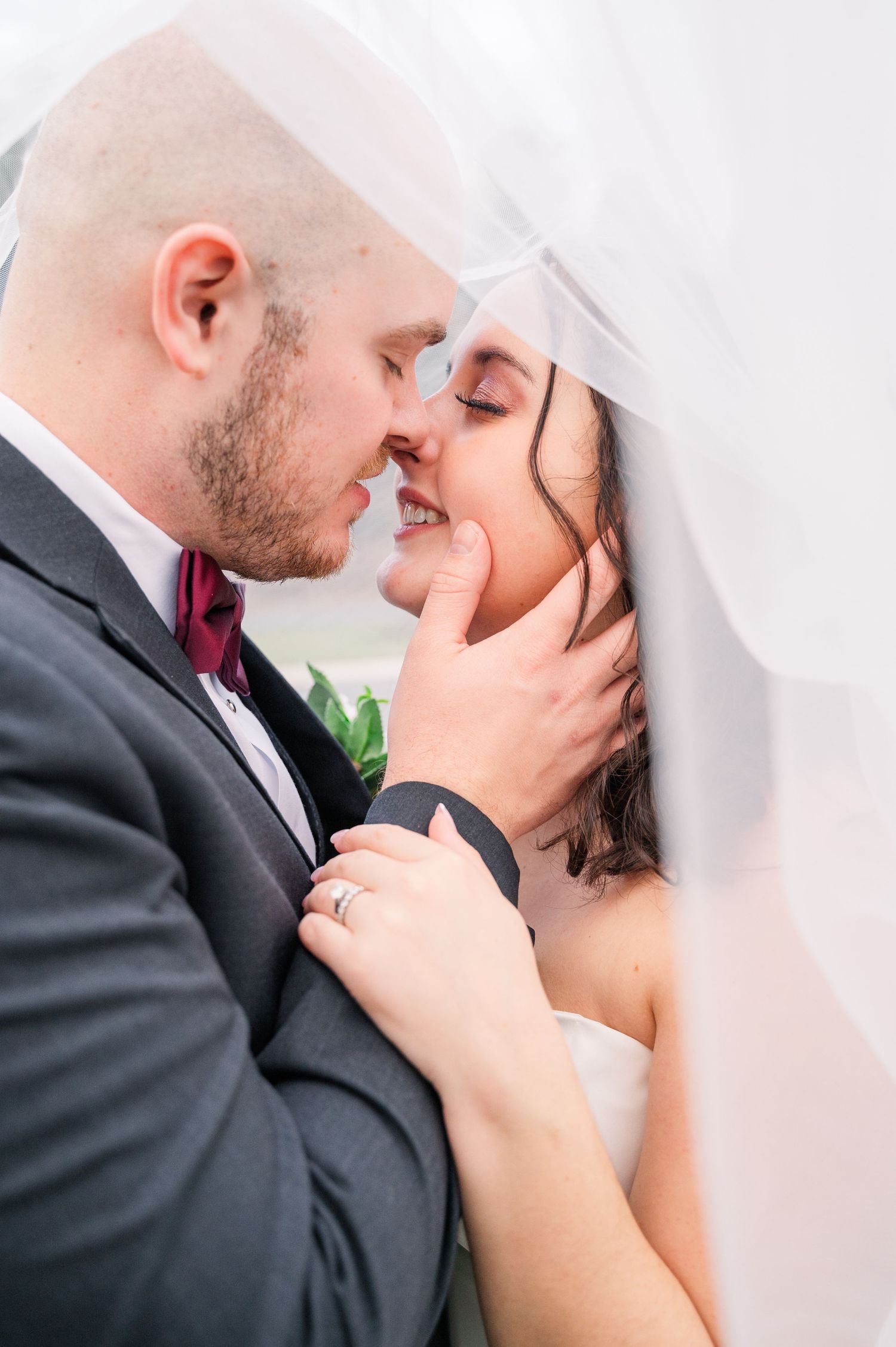 Romantic wedding portrait showing tender moment between newlyweds under a veil.