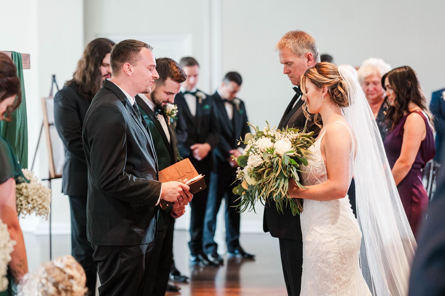 Wedding ceremony guests gather in a bright indoor venue with white walls.