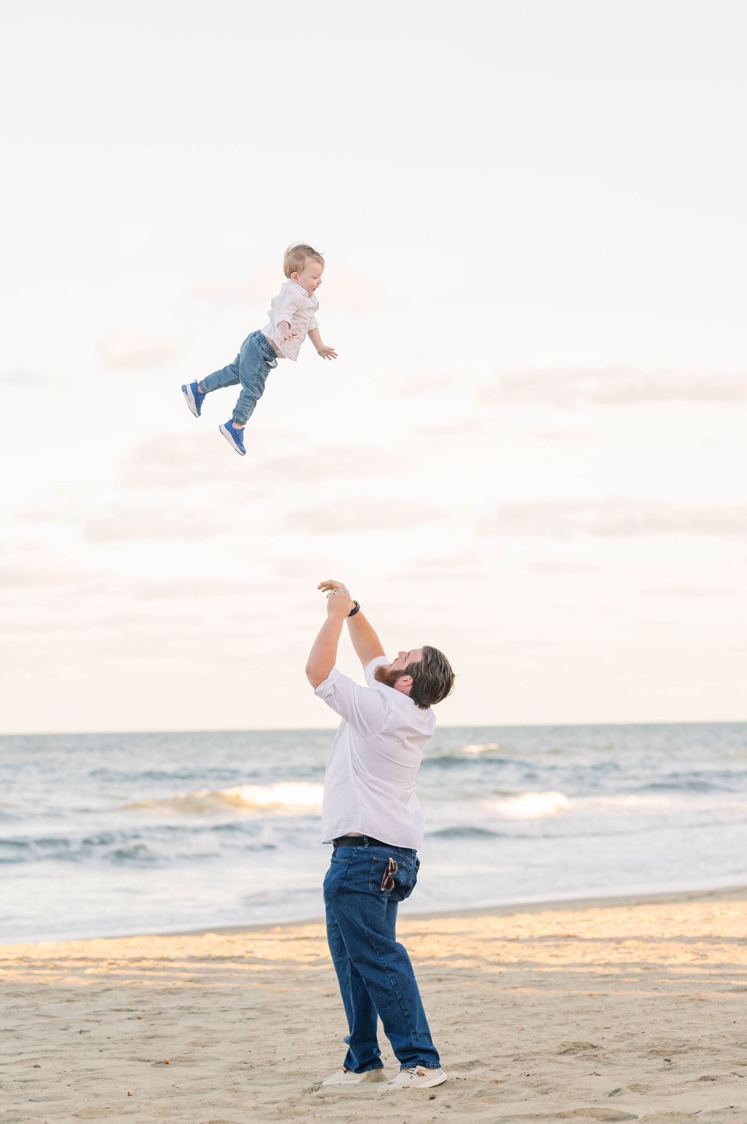 Playful moments captured on beach as child is tossed in air during sunset.